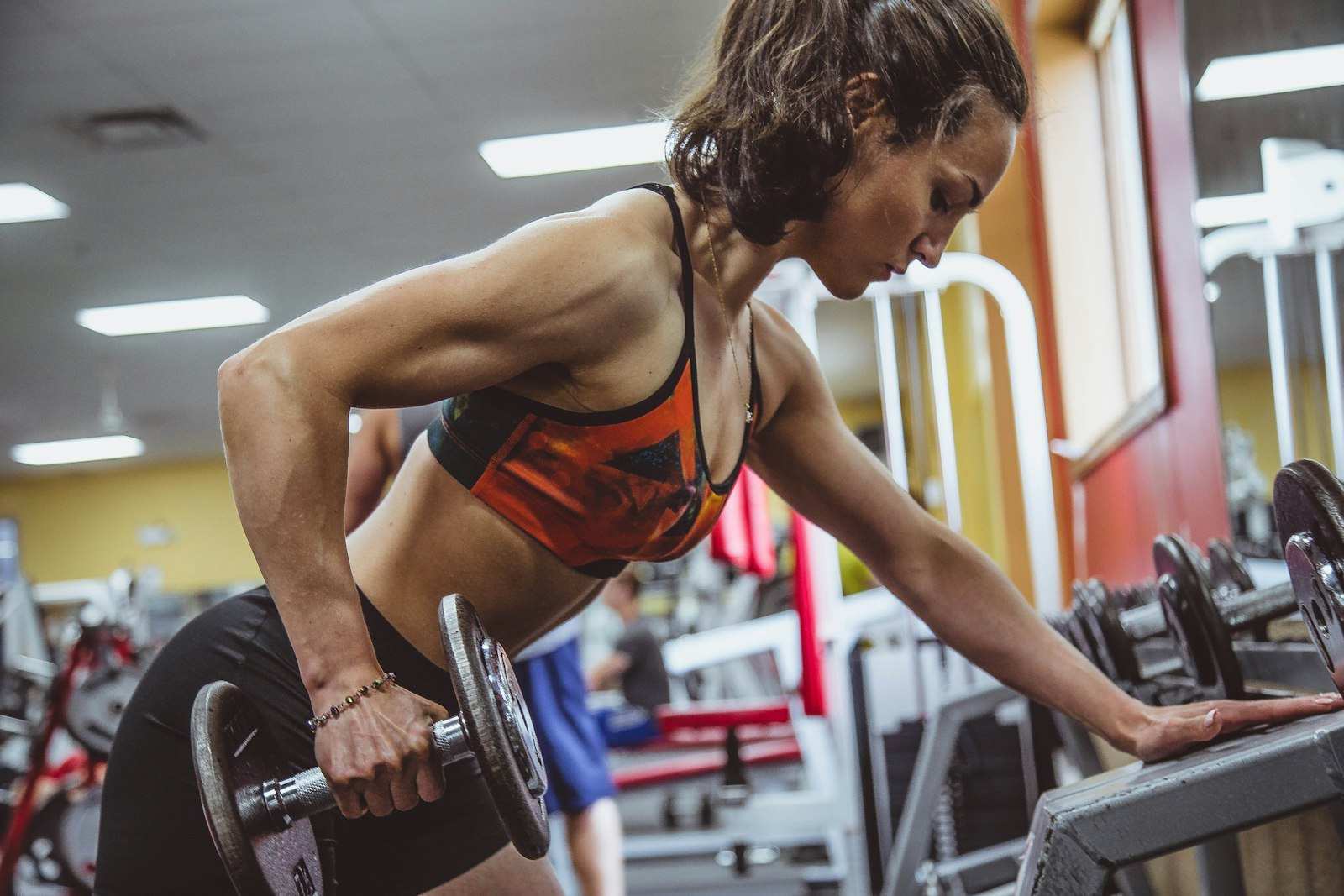 Mujer haciendo remo con mancuerna en el gimnasio